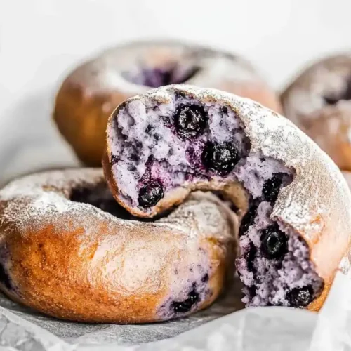 Golden-brown blueberry bagels with a light dusting of flour, showcasing a soft and fluffy interior with juicy blueberries.