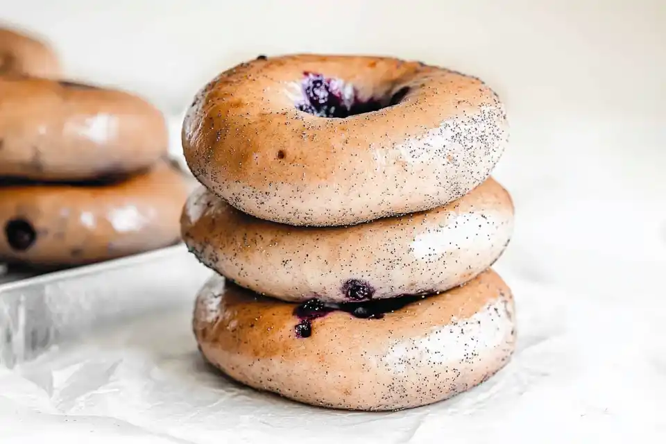 A neatly stacked pile of three freshly baked blueberry bagels with a glossy finish, revealing bits of blueberry inside.