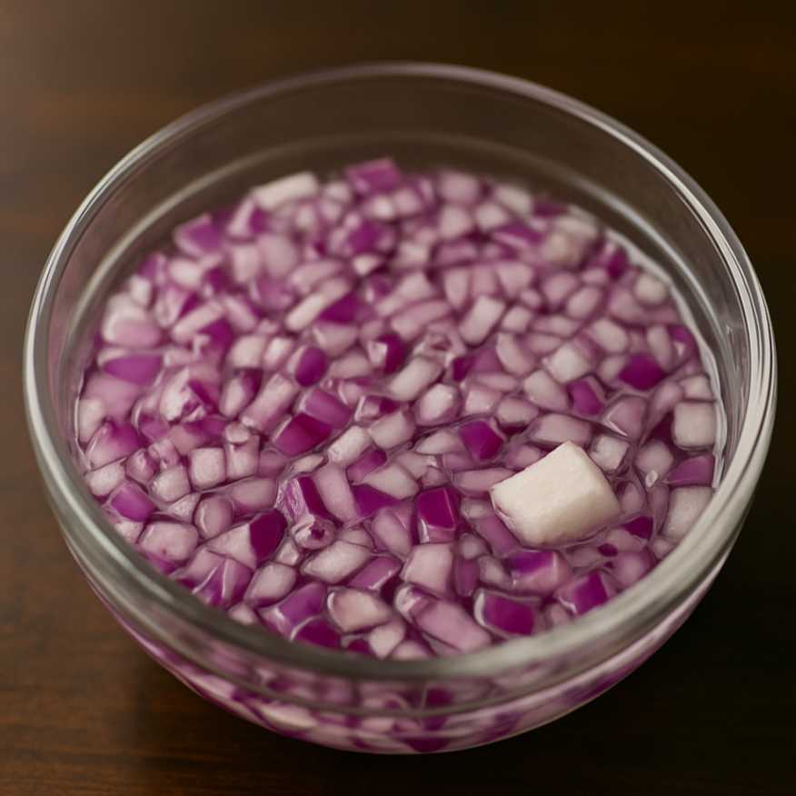 Finely diced red onions soaking in cold water in a glass bowl to reduce sharpness