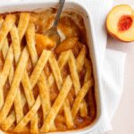 Freshly baked Southern peach cobbler in a white baking dish with a golden lattice crust and warm peach filling, served with a spoon.