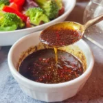 Mediterranean salad dressing with sumac shown in a glass jar, garnished with herbs.