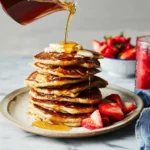 Stack of fluffy oatmeal pancakes topped with fresh fruit and syrup