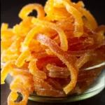 Homemade candied orange peel with a glossy finish on a wooden background.