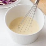 Bowl of homemade coleslaw dressing with fresh ingredients and herbs.