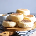 Freshly baked English muffins stacked on a wooden table