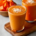 A vibrant Mango Papaya Smoothie in a glass with fresh fruit slices