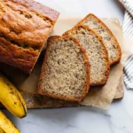 Moist sour cream banana bread with sliced bananas and a cozy kitchen backdrop.