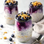 Blueberry cheesecake overnight oats topped with fresh blueberries and cream.