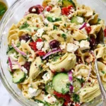 Delicious Greek Pasta Salad with cucumbers, artichoke hearts, and olives in a bowl.