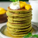 Healthy vegan matcha pancakes stacked on a plate with syrup and berries