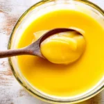 Delicious homemade lemon curd in a glass jar with fresh lemons