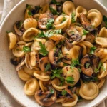 A bowl of spicy miso pasta garnished with herbs and chili flakes.