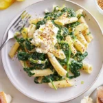 Bowl of creamy spinach feta pasta topped with fresh herbs