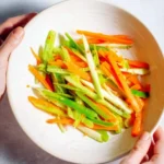 Colorful Asian carrot celery slaw served in a bowl, garnished with sesame seeds.