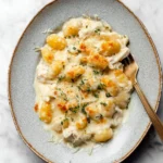 Creamy Chicken Alfredo Gnocchi Bake topped with cheese and herbs