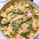 A bowl of creamy salmon asparagus pasta garnished with fresh herbs.