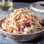 Bowl of creamy sweet coleslaw garnished with fresh herbs
