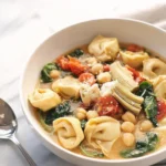 Bowl of creamy tortellini soup with artichokes garnished with herbs