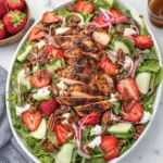 Fresh grilled chicken strawberry salad in a bowl topped with greens and dressing
