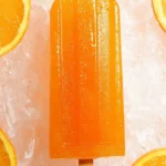 Homemade orange popsicles served on a wooden stick in a sunny setting.
