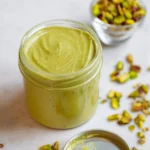 Homemade pistachio cream in a jar with a spoon, perfect for desserts.
