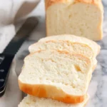 A loaf of freshly baked 2 ingredient milk bread on a wooden cutting board.