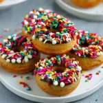 Healthy banana protein donuts on a plate, topped with nuts and chocolate drizzle.
