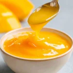 Delicious homemade mango sauce in a bowl with fresh mangoes around it.