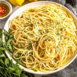 Plate of spaghetti with olive oil, garlic, and fresh herbs on a rustic table