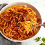Plate of pasta topped with rich tomato butter sauce and fresh herbs.