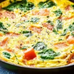 Easy spinach and tomato frittata on a plate, garnished with fresh spinach.