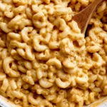 A bowl of healthy mac and cheese topped with fresh herbs and vegetables.