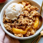 Bowl of healthy peach crisp topped with fresh peaches and oats