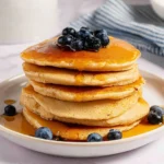 Fluffy oat flour pancakes stacked on a plate with syrup and berries
