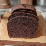 Freshly baked Pumpernickel Bread slices on a wooden cutting board.