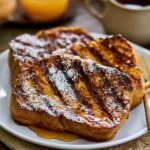 Delicious grilled French toast served with fruits and syrup on a plate.