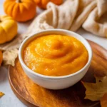 Homemade pumpkin puree in a bowl with fresh pumpkins in the background.