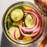 A jar of pickled cucumbers and onions on a wooden table.