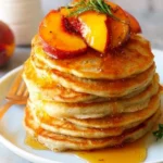 Delicious buttermilk peach pancakes stacked on a plate drizzled with syrup