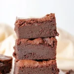 Fudge brownies topped with cream cheese frosting on a white plate